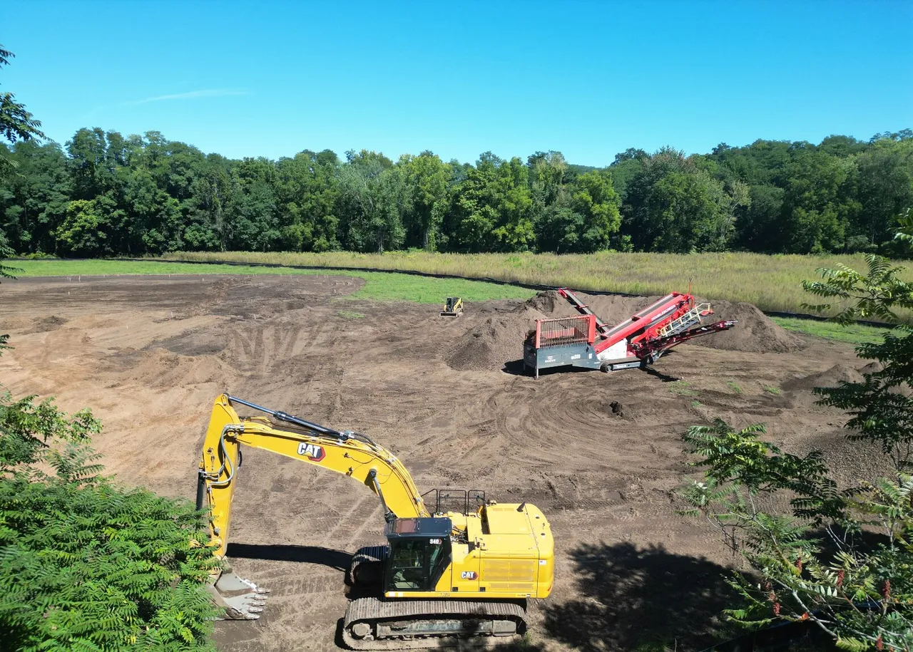 Drone view of the excavator on a cleared site with the topsoil screener behind it