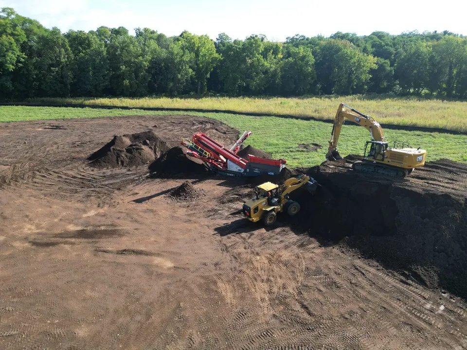 Drone view of an excavator and loader feeding the topsoil screener on a large grading site