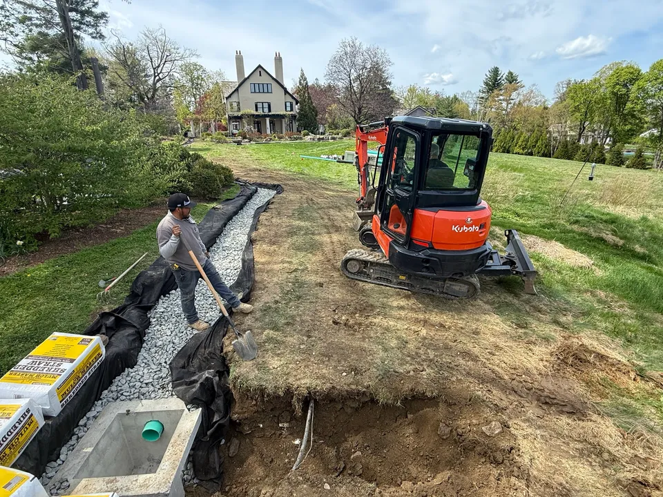Backfilling a drain trench with stone beside a new catch basin