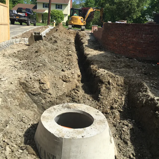 Concrete dry well structure set in a trench beside a brick wall