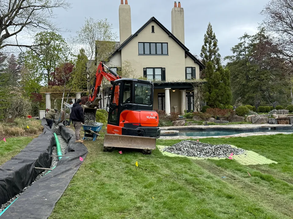 French drain trench cut across an estate yard toward the house
