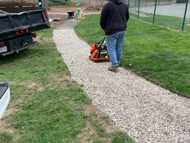 Compacting a new gravel path beside a tennis court
