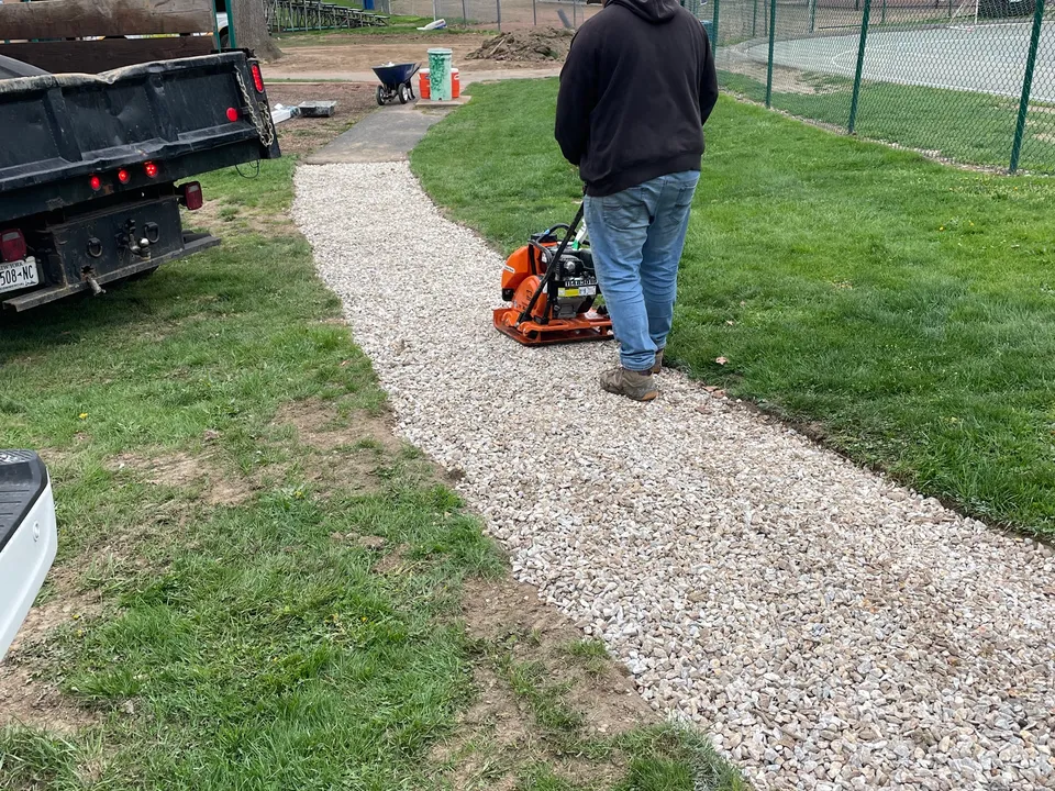 Compacting a new gravel path beside a tennis court