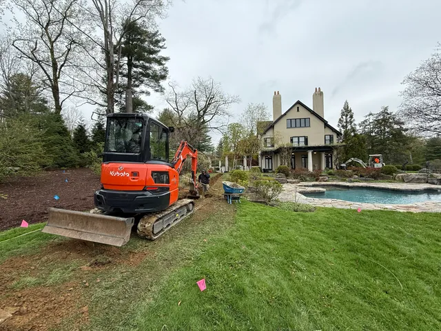 Mini excavator trenching a yard for drainage beside a pool