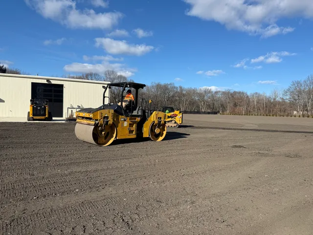 Roller compacting a new gravel lot beside a warehouse