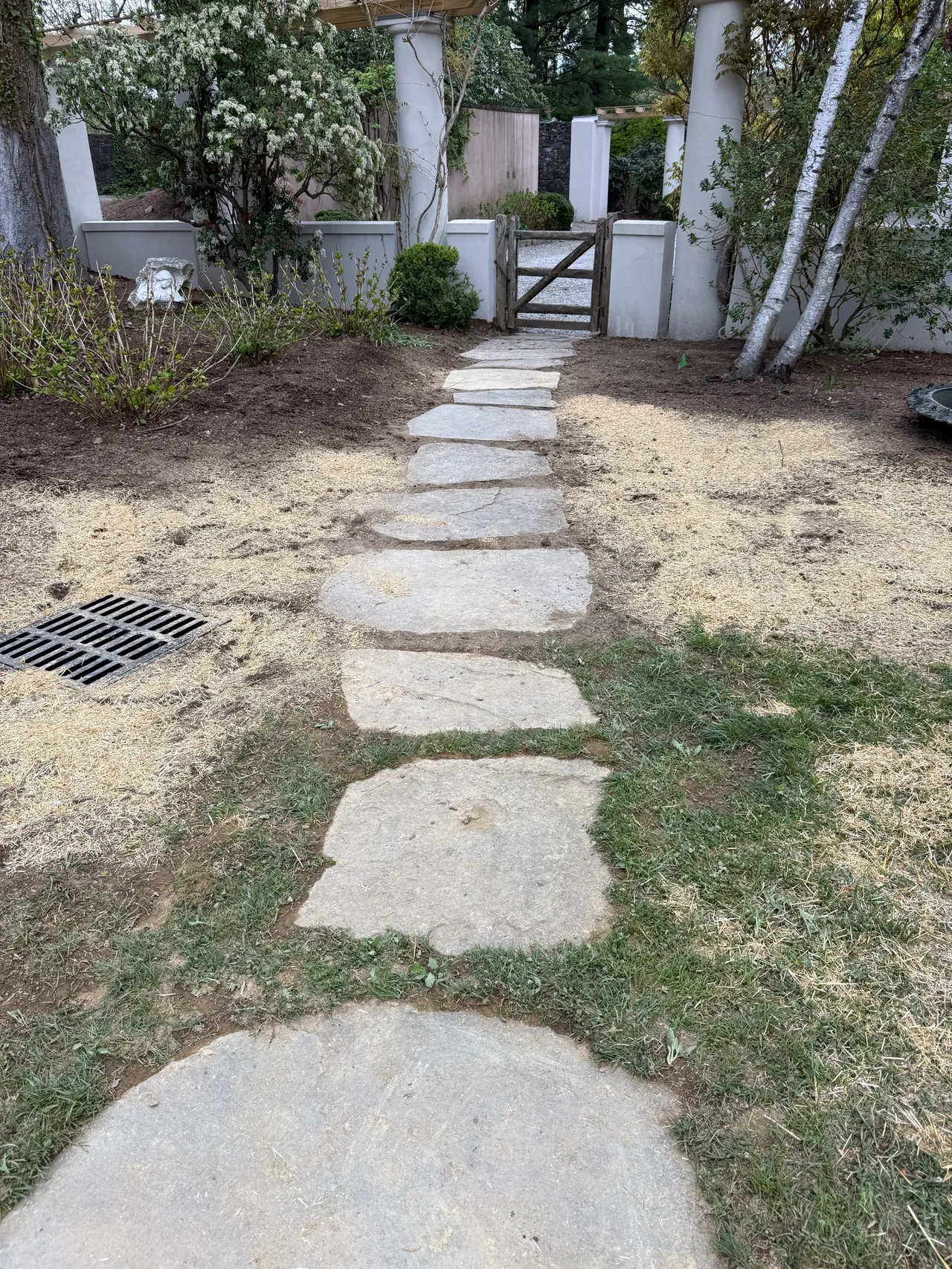 Stone stepping path with a drain grate at a garden gate