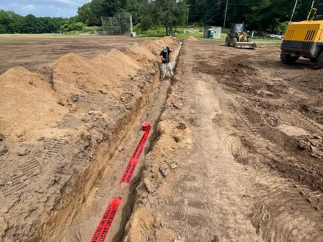 Trench with red conduit running across a field